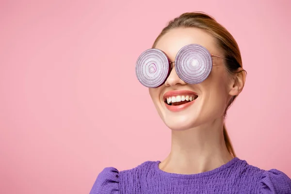 Femme souriante portant des lunettes avec des anneaux d'oignon violet isolé sur rose, concept de surréalisme — Photo de stock
