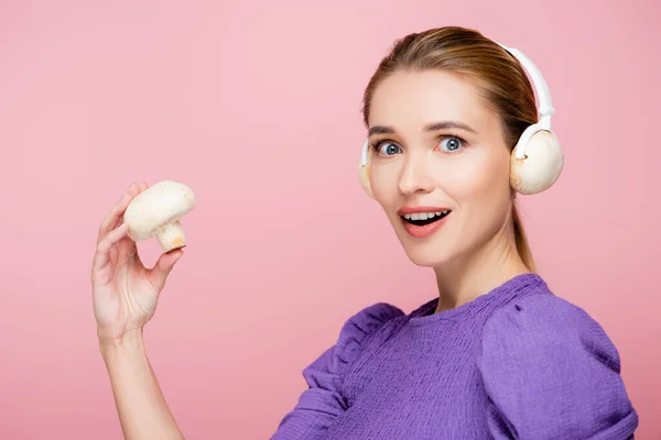 Excited woman with mushrooms in headphones holding champignon isolated on pink — Stock Photo