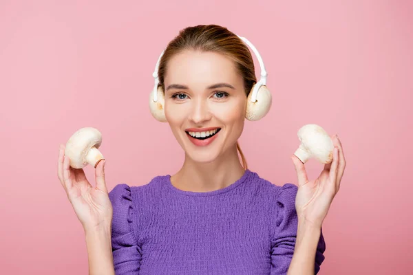 Smiling woman with mushrooms in headphones holding champignons isolated on pink — Stock Photo