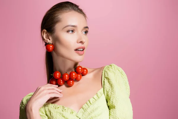 Mulher sensual no colar de tomates cereja vermelho olhando para longe isolado em rosa — Fotografia de Stock
