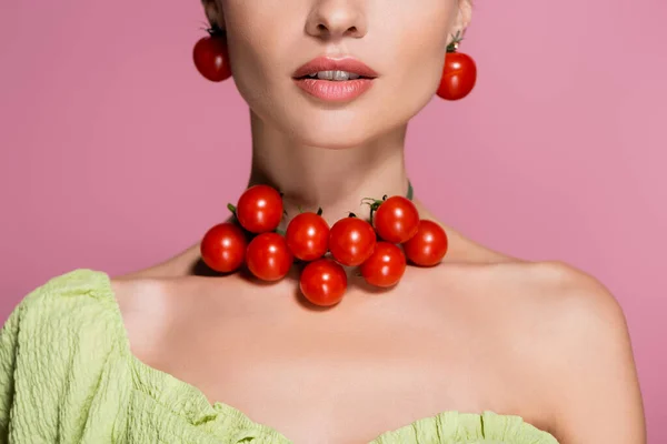 Vue partielle de jeune femme en tomates cerises rouges boucles d'oreilles et collier isolé sur rose — Photo de stock