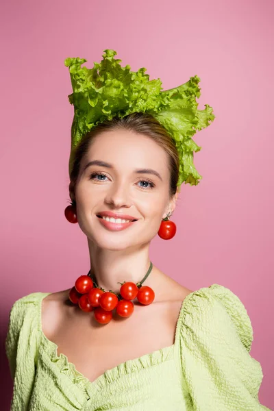 Femme heureuse en collier, boucles d'oreilles et chapeau en légumes souriant à la caméra sur rose — Photo de stock