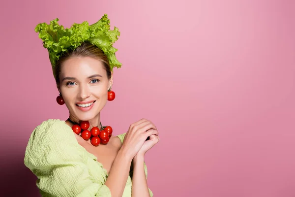 Femme souriante en chapeau, collier et boucles d'oreilles en légumes posant sur rose — Photo de stock