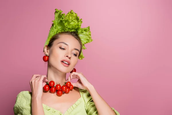 Encantadora mujer en sombrero de lechuga, tocando collar loco de tomates alegres en rosa - foto de stock