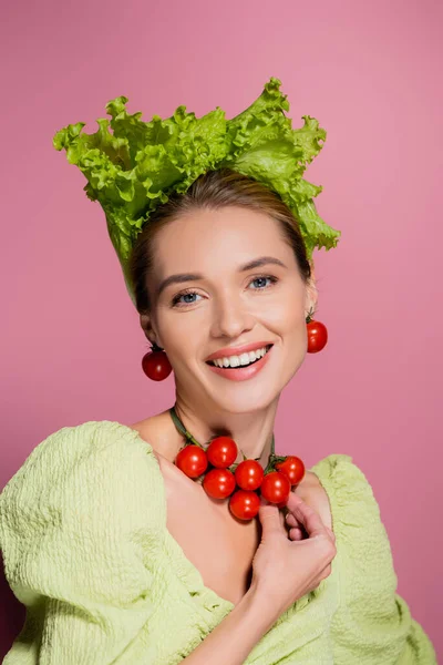 Heureuse jeune femme en laitue chapeau touchant collier en tomates cerises sur rose — Photo de stock