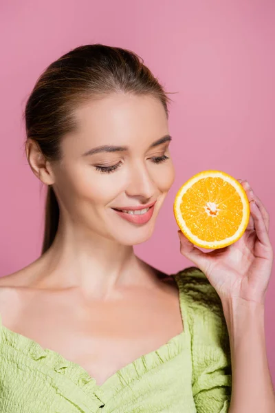 Гарна жінка з натуральним макіяжем тримає половину стиглого апельсина ізольовано на рожевому — стокове фото