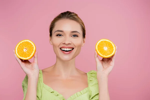 Excited woman with natural makeup holding halves of fresh orange isolated on pink — Stock Photo