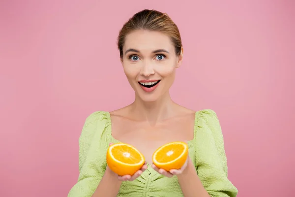 Amazed woman holding halves of ripe fresh orange isolated on pink — Stock Photo