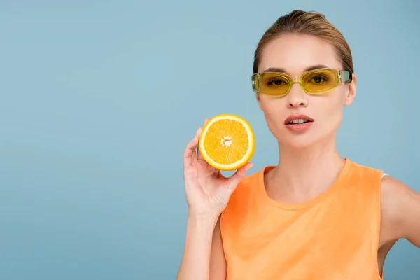 Очаровательная женщина в цветных очках позирует с половиной спелого апельсина изолированы на синий — стоковое фото