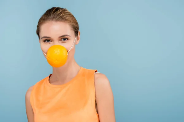 Mujer joven con máscara de seguridad hecha de naranja medio aislado en azul - foto de stock