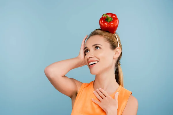 Excited woman with red bell pepper instead of hat posing with hand on chest isolated on blue — Stock Photo