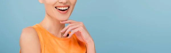 Vista cortada de mulher sorridente posando com a mão perto do queixo isolado em azul, banner — Fotografia de Stock