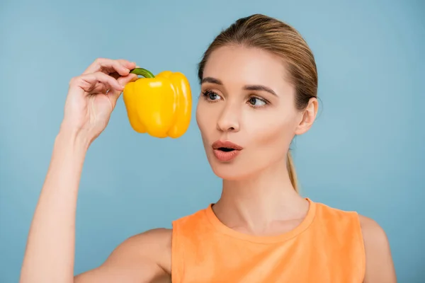 Verblüffte Frau mit natürlichem Make-up mit reifer gelber Paprika isoliert auf blau — Stockfoto