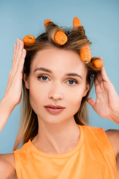Jolie femme avec maquillage naturel en utilisant des carottes comme bigoudis isolés sur bleu — Photo de stock