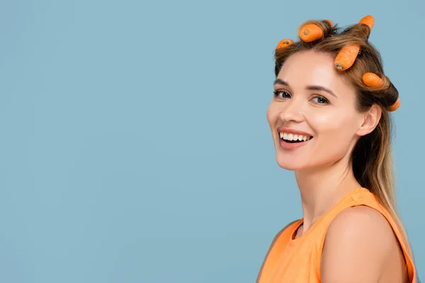 Jeune femme heureuse utilisant des carottes au lieu de bigoudis isolés sur bleu — Photo de stock