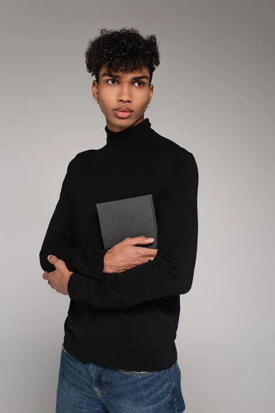 Pierced african american man in turtleneck sweater holding notebook isolated on grey — Stock Photo