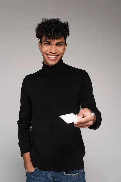 Hombre afroamericano feliz en jersey de cuello alto dando tarjeta en blanco aislado en gris - foto de stock
