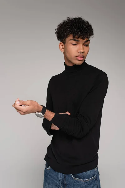 Giovane uomo africano americano che regola la manica sul maglione collo alto isolato sul grigio — Foto stock