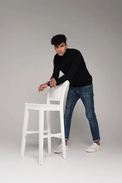 Pleine longueur de jeune homme afro-américain posant près de chaise sur gris — Photo de stock