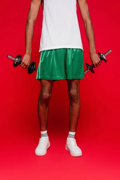Vista cortada do homem americano africano esportivo em shorts e top tank exercitando com halteres em vermelho — Fotografia de Stock