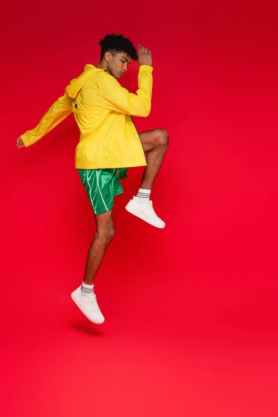 Longitud completa del hombre afroamericano deportivo en chaqueta amarilla trabajando en rojo - foto de stock
