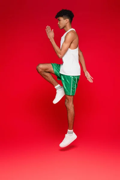 Full length of sportive african american man in green shorts working out on red — Stock Photo