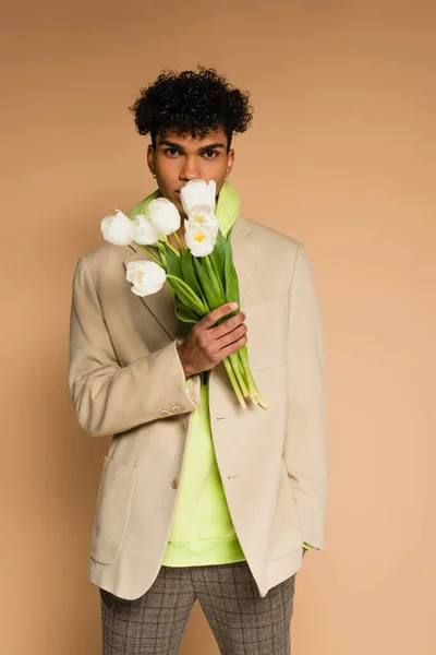 African american man in hoodie and blazer holding tulips on beige — Stock Photo