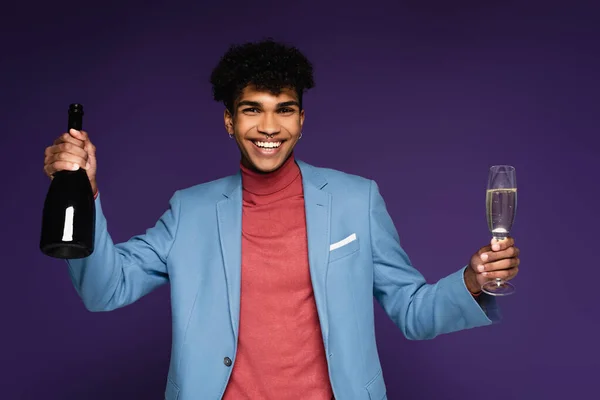 Afrikanisch-amerikanischer Mann im blauen Blazer mit Glas und Champagnerflasche auf lila — Stockfoto