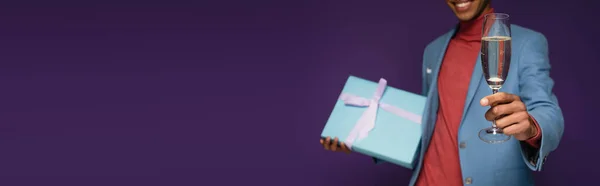 Частичный вид веселого африканского американца с бокалом шампанского и присутствующего на фиолетовом баннере — стоковое фото