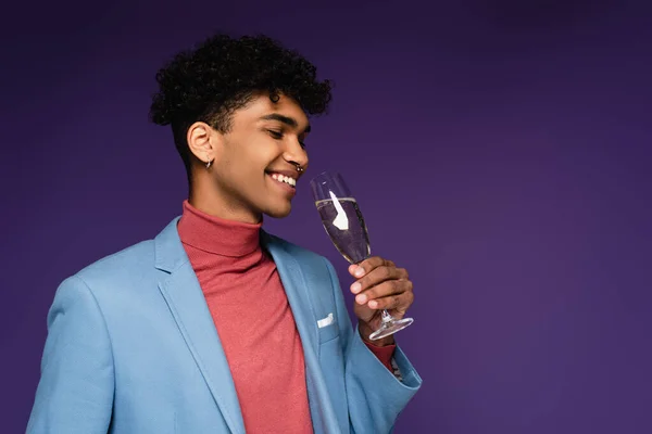 Lockiger afrikanisch-amerikanischer Mann im blauen Blazer, der ein Glas Champagner hält, während er auf lila lächelt — Stockfoto