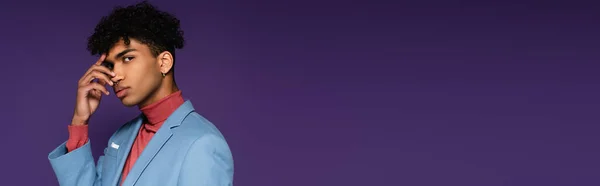 Пронзительный африканский американец в синем блейзере смотрит в камеру, позируя на фиолетовом баннере — стоковое фото