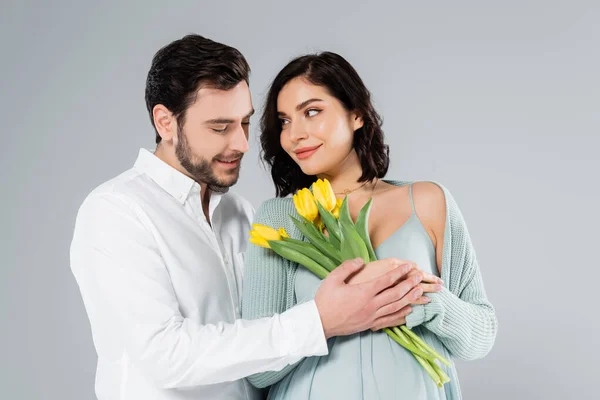 Femme enceinte tenant des tulipes près d'un mari souriant isolé sur gris — Photo de stock