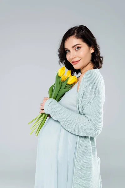 Femme enceinte avec des tulipes jaunes regardant la caméra isolée sur gris — Photo de stock