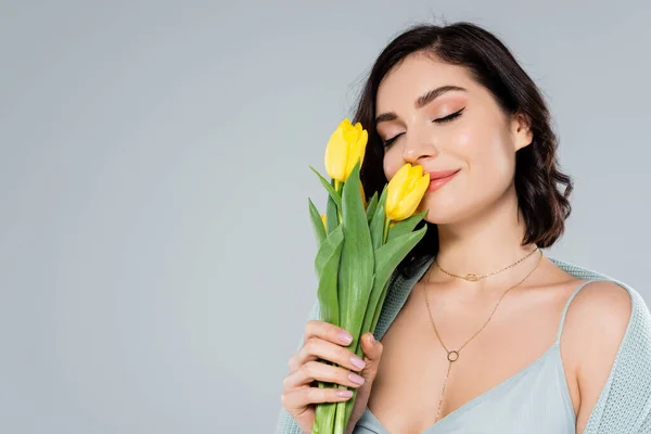 Молода жінка пахне жовтими тюльпанами ізольовані на сірому — стокове фото