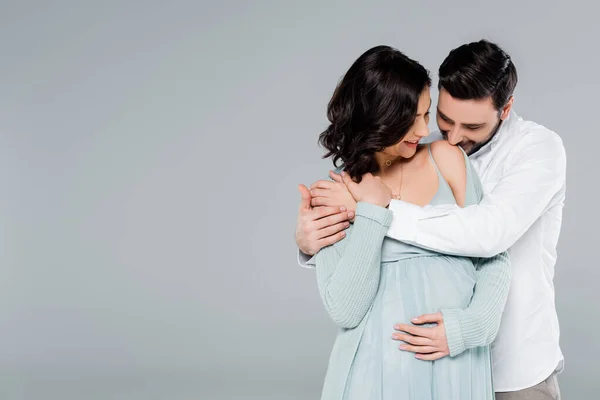 Man kissing shoulder of pregnant wife isolated on grey — Stock Photo