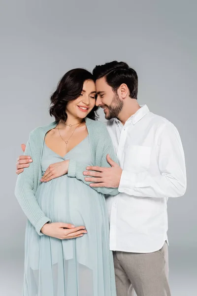 Uomo abbracciando sorridente moglie incinta isolato su grigio — Foto stock