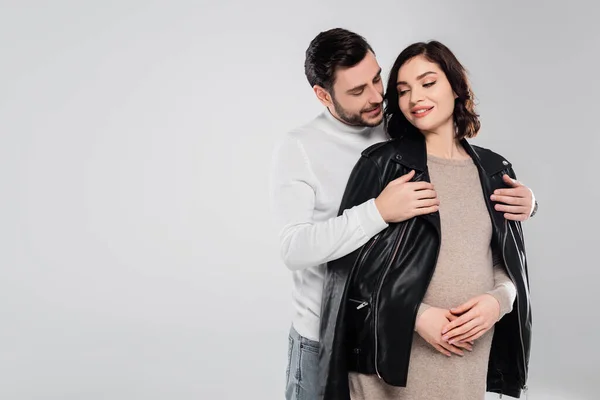 Sonriente hombre usando chaqueta en joven embarazada esposa aislado en gris - foto de stock