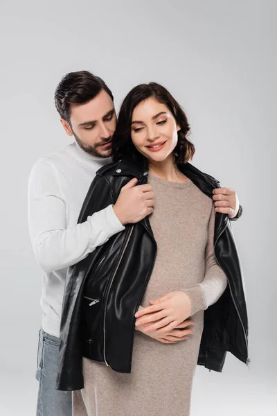 Hombre con chaqueta en mujer embarazada sonriente aislado en gris - foto de stock