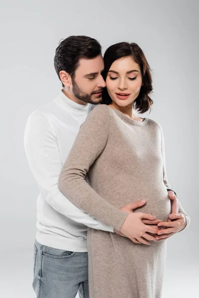 Man hugging pregnant wife in dress isolated on grey — Stock Photo