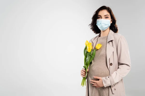 Schwangere in medizinischer Maske hält Tulpen isoliert auf grau — Stockfoto