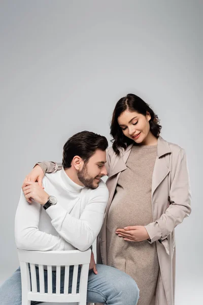 Усміхнена пара дивиться на живіт вагітної жінки ізольовано на сірому — стокове фото