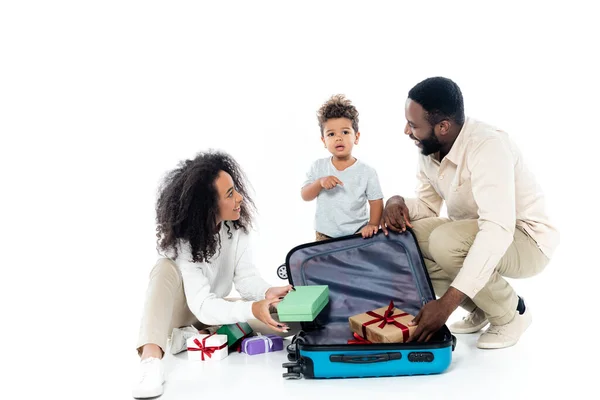 African american boy pointing at suitcase near happy parents on white — Stock Photo