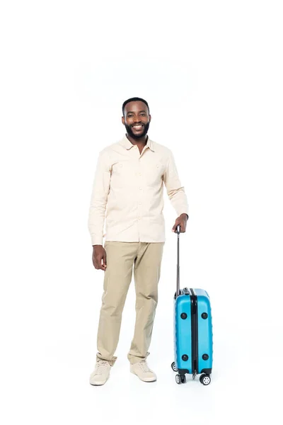 Hombre afroamericano feliz mirando a la cámara mientras está de pie con la bolsa de viaje en blanco - foto de stock