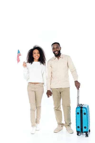 Щаслива афроамериканська жінка тримає маленький прапор США біля чоловіка з валізою на білому — стокове фото