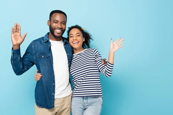Joyful african american couple waving hands at camera isolated on blue — Stock Photo