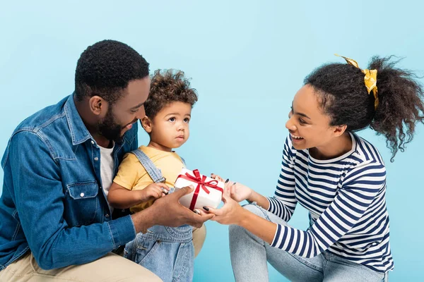 Gioiosi genitori afro-americani che presentano dono al figlio isolato sul blu — Foto stock