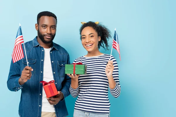 Smiling african american couple holding gift boxes and small flags of usa on blue — Stock Photo