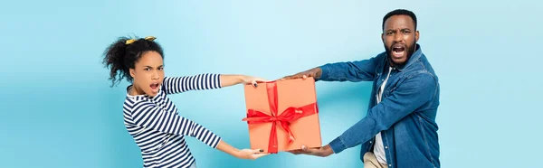 Furiosa pareja afroamericana quitándose la caja de regalo en azul, pancarta - foto de stock