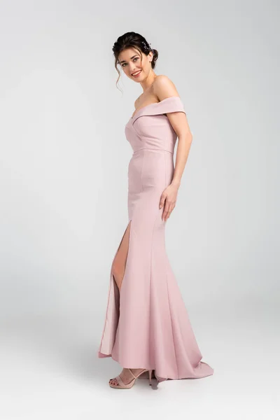 Full length view of woman in pink, elegant dress smiling at camera on grey — Stock Photo
