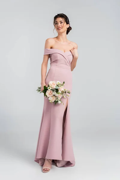 Full length view of elegant fiancee looking away while holding wedding bouquet on grey — Stock Photo